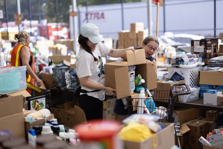 Two people dump box of supplies into shopping cart