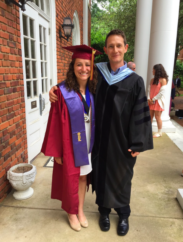 A woman in a maroon cap and gown with a male professor in a doctorate hood