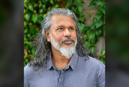 Shehan Karunatilaka in a blue shirt next to an ivy-covered wall