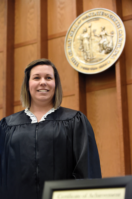 A female judge stands behind the bench in a courtroom and smiles