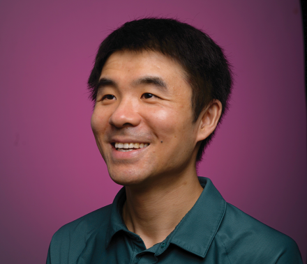 A male faculty member looks off camera and smiles against a purple backdrop