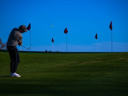 Person hits a golf ball with flags in the background