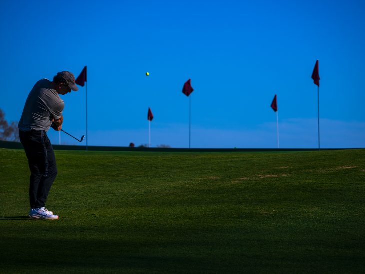 Person hits a golf ball with flags in the background