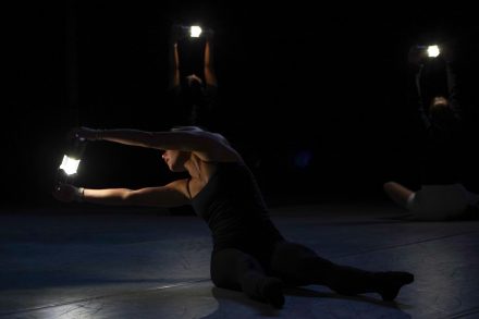 three dancers dressed in black holding LED lanterns while moving onstage