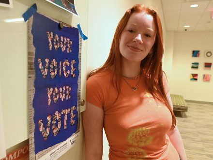 Communication design major Hannah Israel '25 of Elon University stands with voting poster.