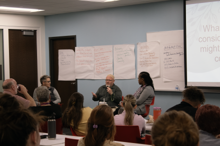 Three people talk at the front of a room