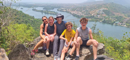 A husband and wife and their three children sit on a rock with a Ghanian landscape behind them.