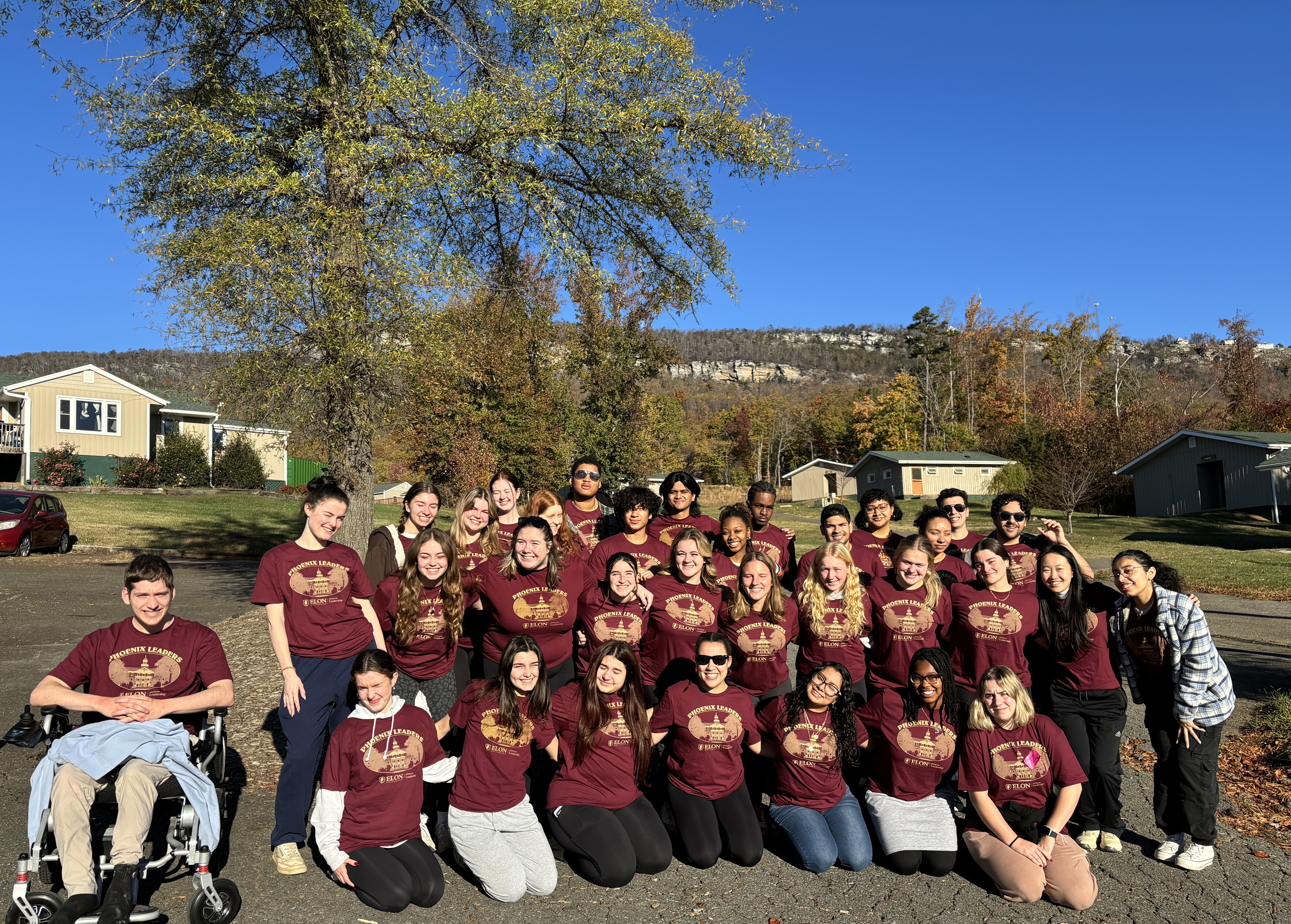 Group of college students smiling in front of cabins and mountains