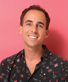 A man smiles at the camera in a professional headshot against a pink backdrop