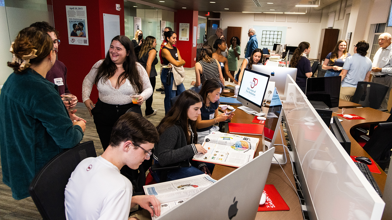 Alumni and students of the Pendulum look at archives in the newsroom.