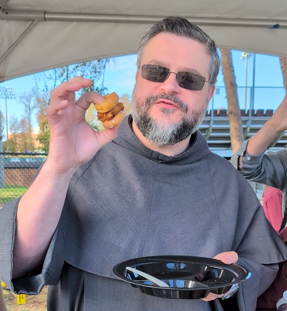 Father Peter holding a sandwich of a chicken nugget and donut holes