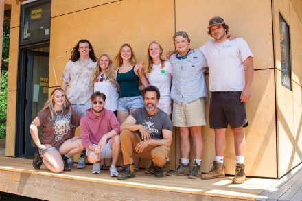 Several male and female students stand in front of the structure they designed and built in the EcoVillage at Loy Farm