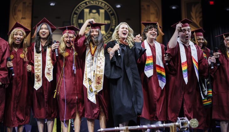 Several people in caps and gowns cheer on stafe