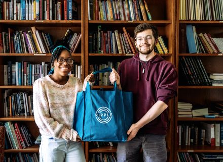 Morgan Williams and Ryan Gibbons hold a bag between them in front of a bookshelf.