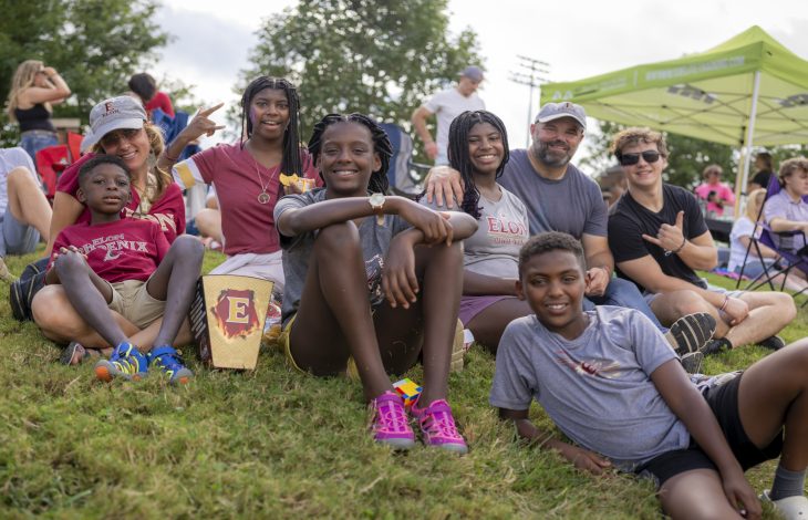 A group of people sit on grass and smile