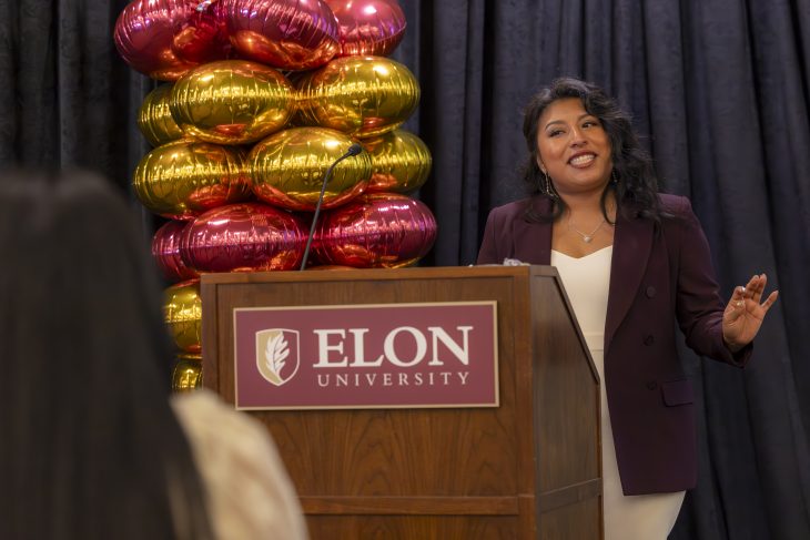 Woman stands behind Elon podium and speaks with maroon and gold balloons to her left