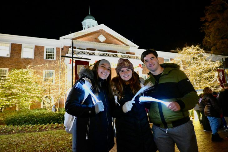 Three people stand in front of Alamance Building with glow sticks