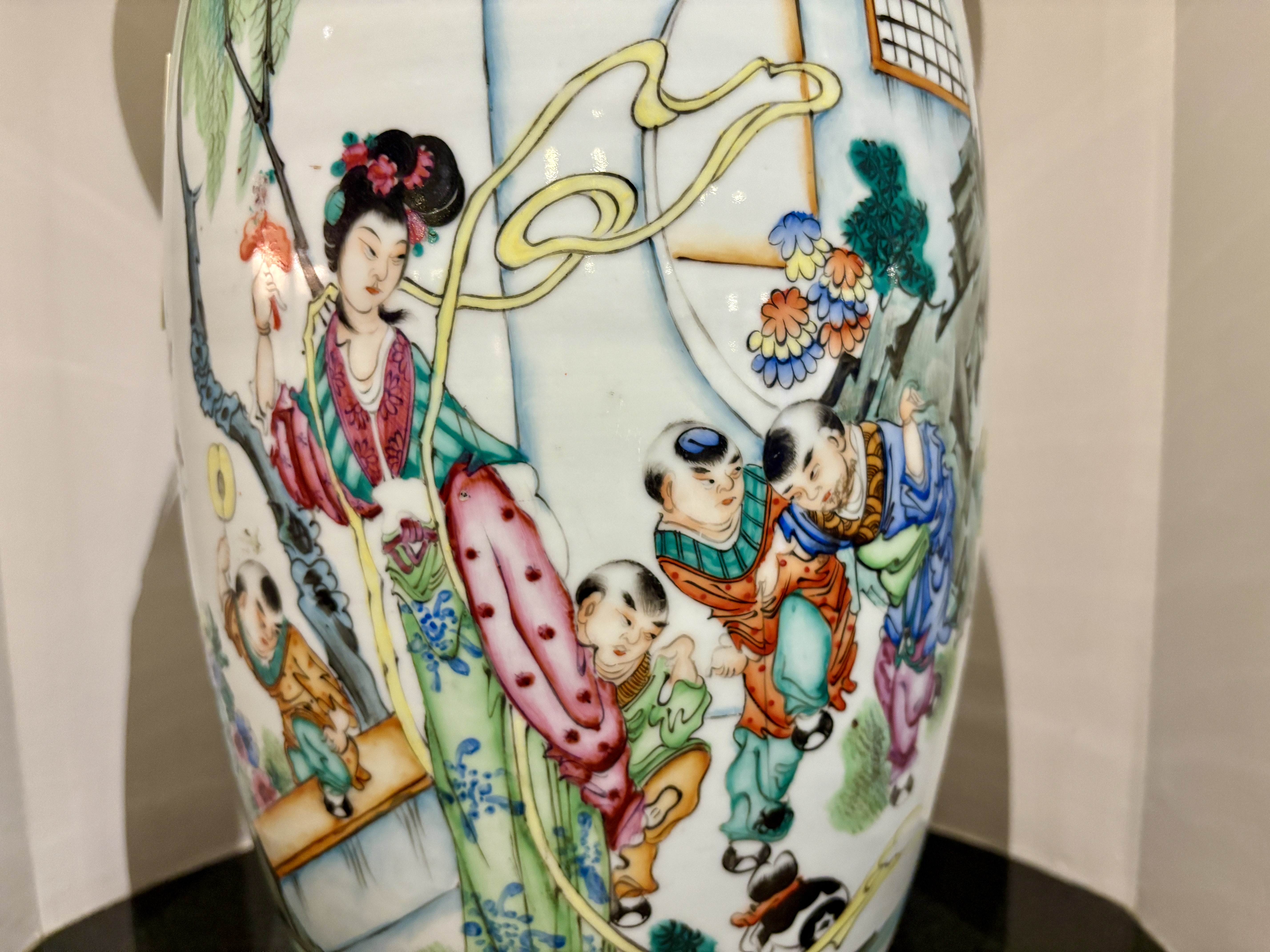 Close-up of a Chinese porcelain vase with intricate painted designs depicting a woman and children in traditional attire surrounded by floral elements.