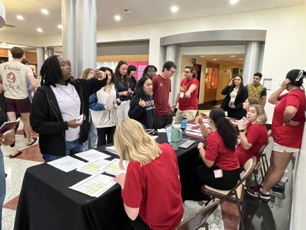 Attendees gather at the registration table for the 2024 Intersect Conference in a busy lobby. Volunteers in red T-shirts assist with name tags and schedules, while attendees wait in line, some engaging in conversations. The scene is energetic, with various individuals standing and sitting near the table.