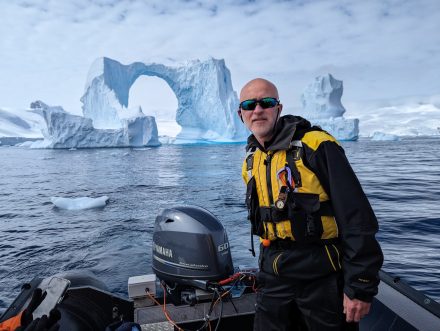 A man in a small boat with icebergs and glaciers behind him