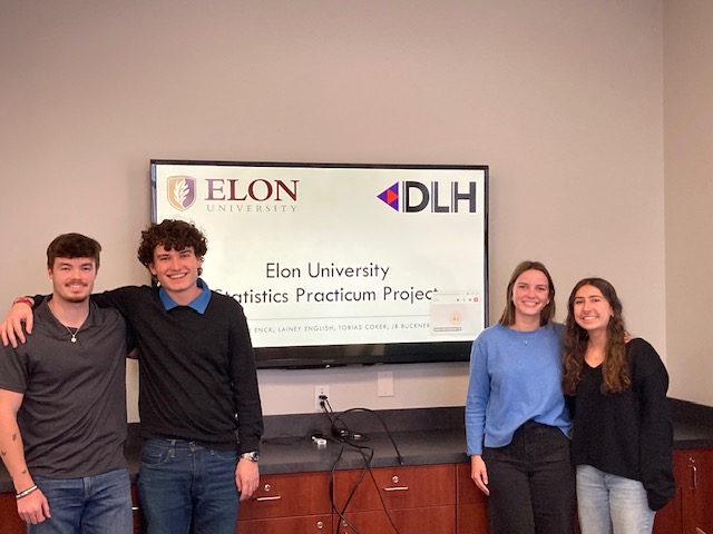 Four students pose for photo in front of a TV