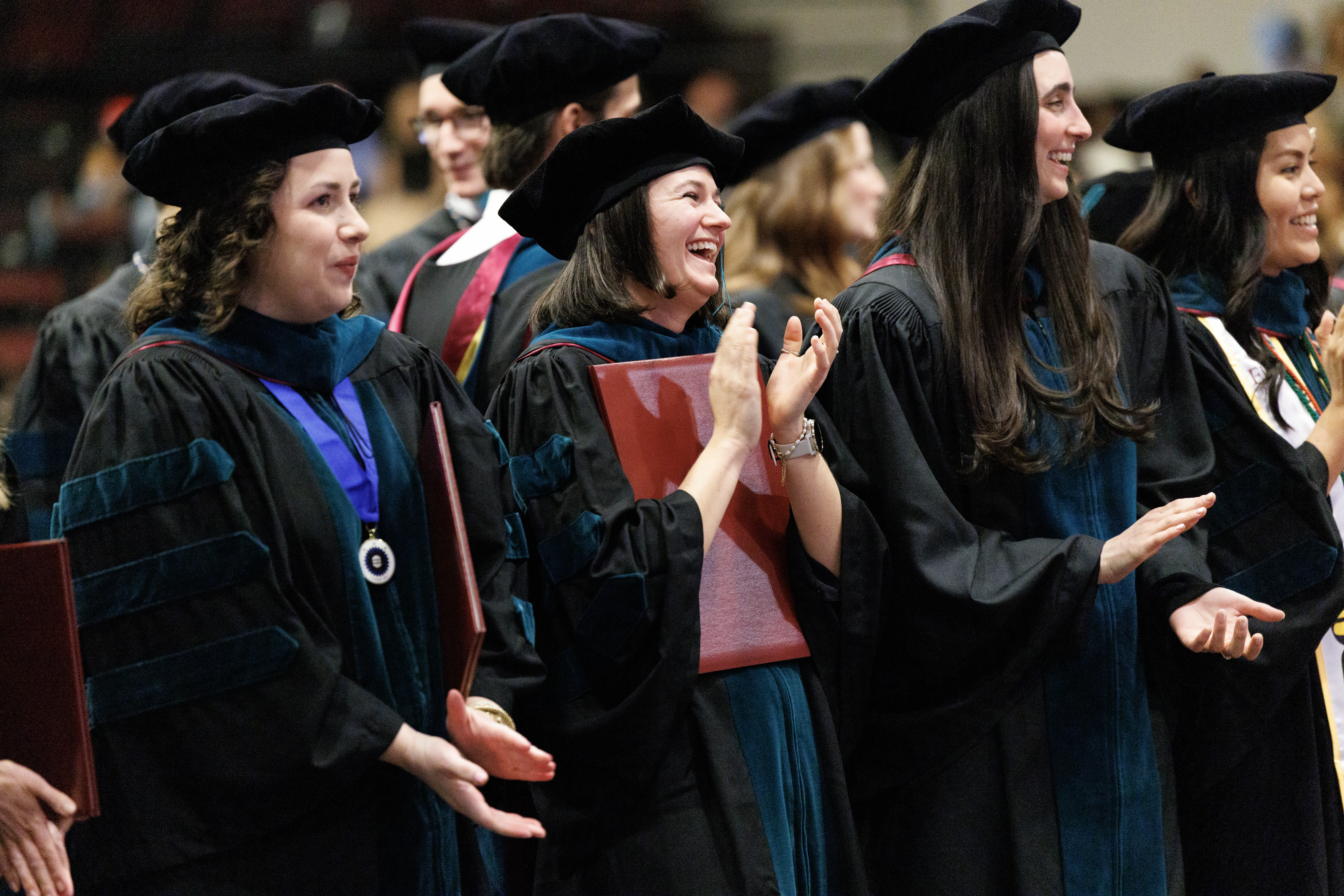 Three people in regalia clap and smile