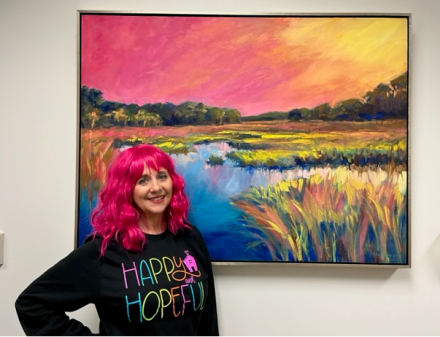 Woman with pink hair stands in front of artwork