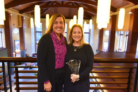 Two people pose for photo. Woman on the right holds a trophy