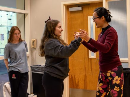 A professor and female student dance face to face with their hands together , smiling.