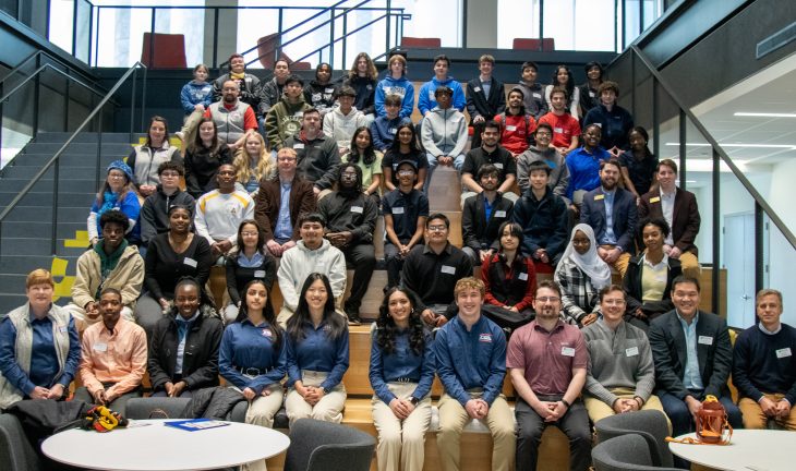 A large group of middle and high school students with teachers and Elon faculty and staff seated on the stairs in Hunt Atrium