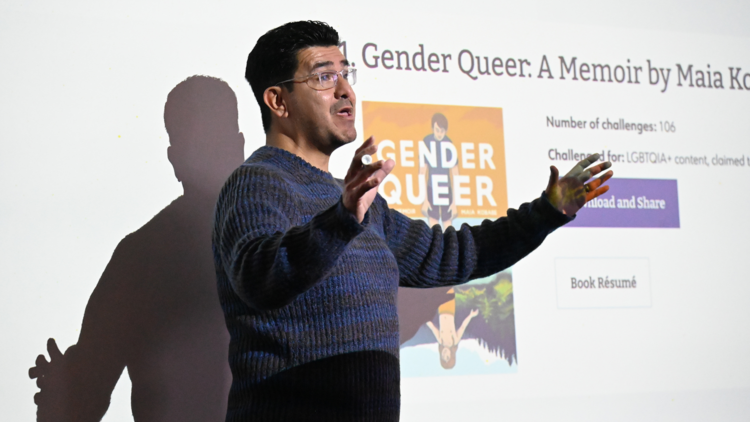 Elon professor Israel Balderas stands in front of a Powerpoint presentation.