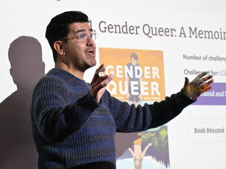 Elon professor Israel Balderas stands in front of a Powerpoint presentation.