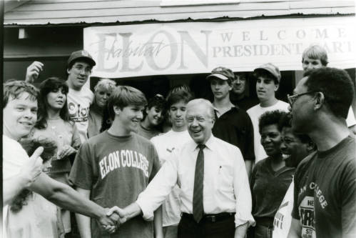 Group of smiling people greeting President Jimmy Carter under a banner that reads "Welcome President Carter."