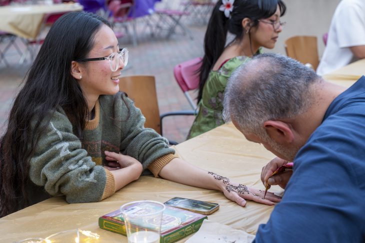 Person getting a henna design applied on their hand by an artist at an outdoor event.