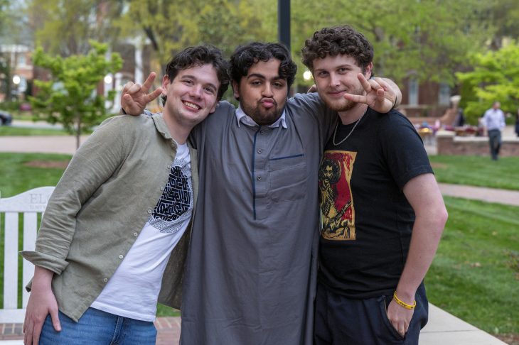 Three friends posing together with peace signs in a park-like setting.
