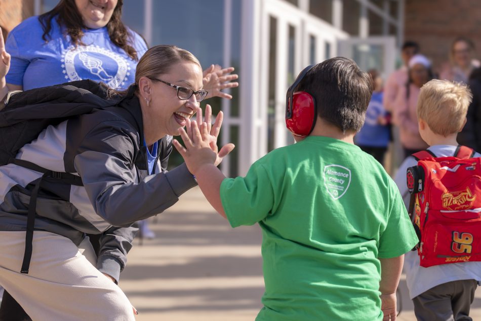 Two individuals happily high-fiving outside a school, with one person wearing a backpack.