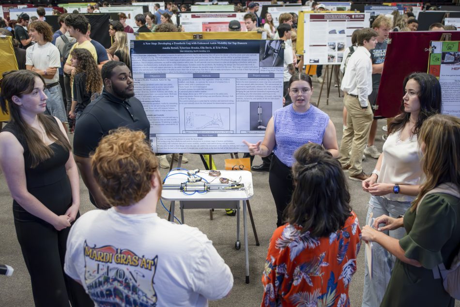 A group of people engaged in discussion at a science fair, with one individual presenting a project