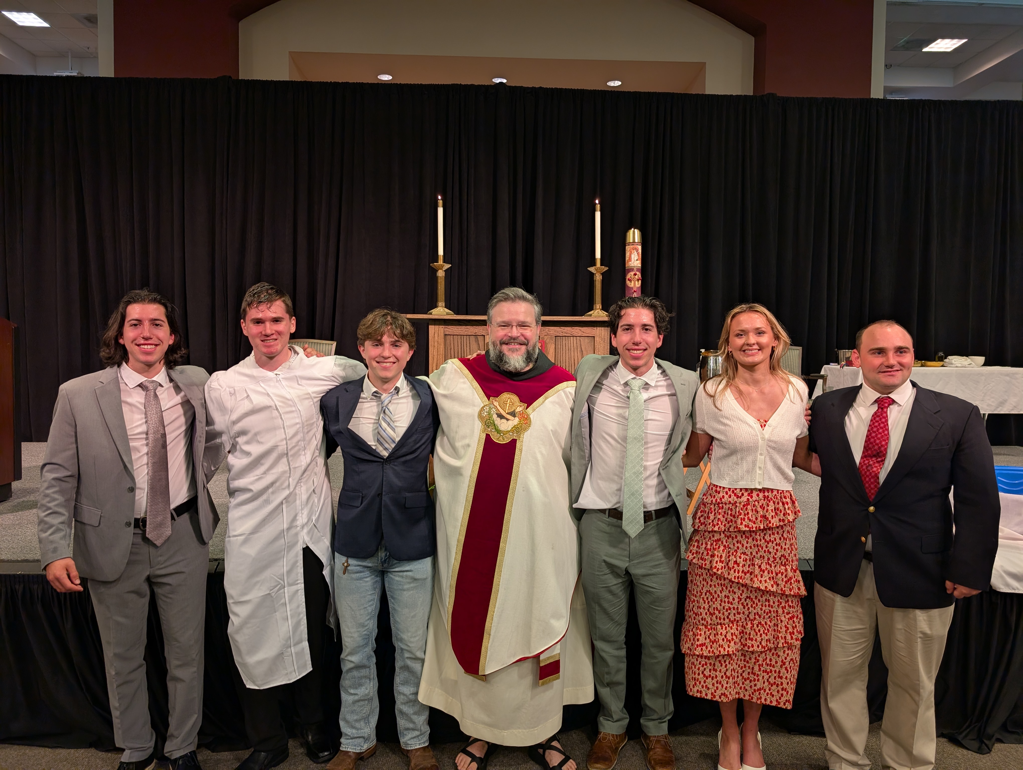 Seven people pose for a photo. The middle person is wearing priest atire.