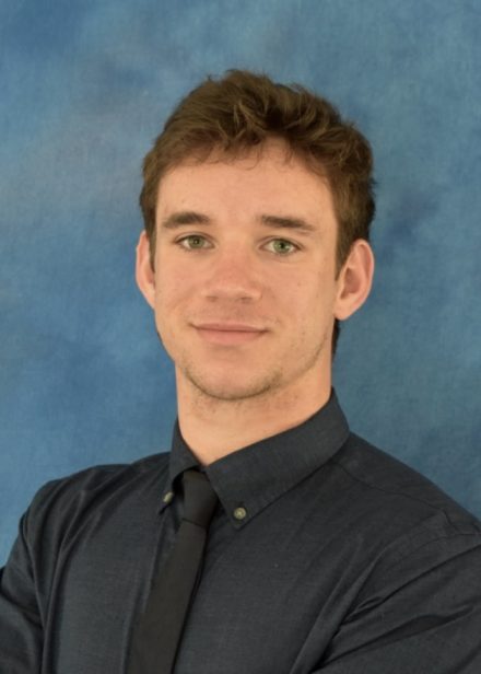 A headshot of Chris D'Inzeo '24 in a black shirt and black tie against a blue background.