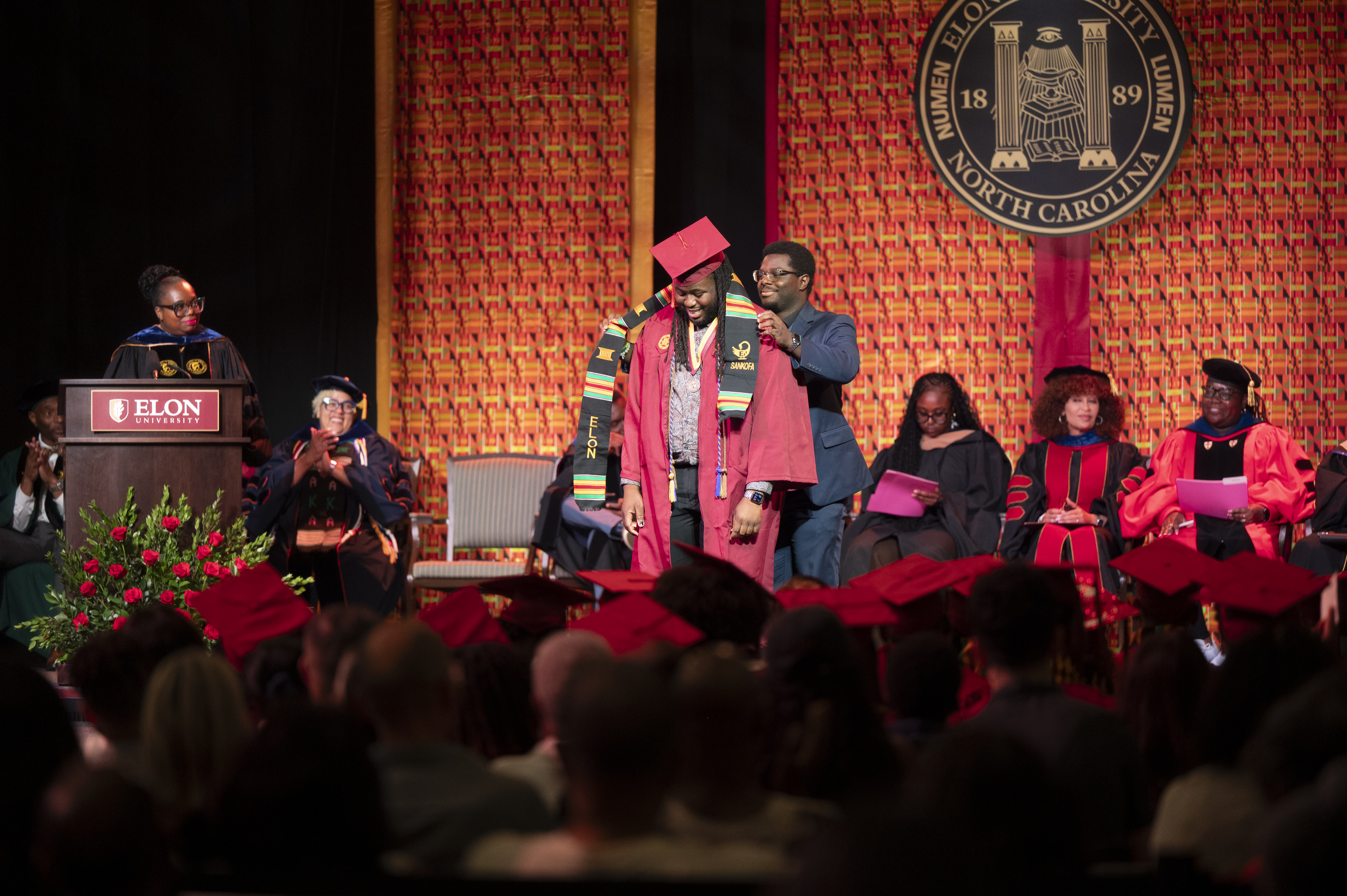 A kente cloth stole is being placed on the shoulders of a graduating senior.