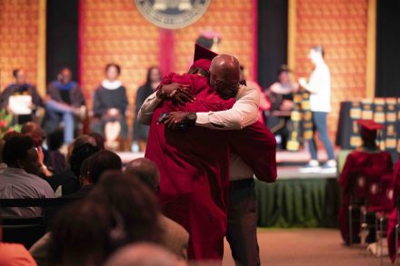 A graduating senior embraces his father in the aisle.