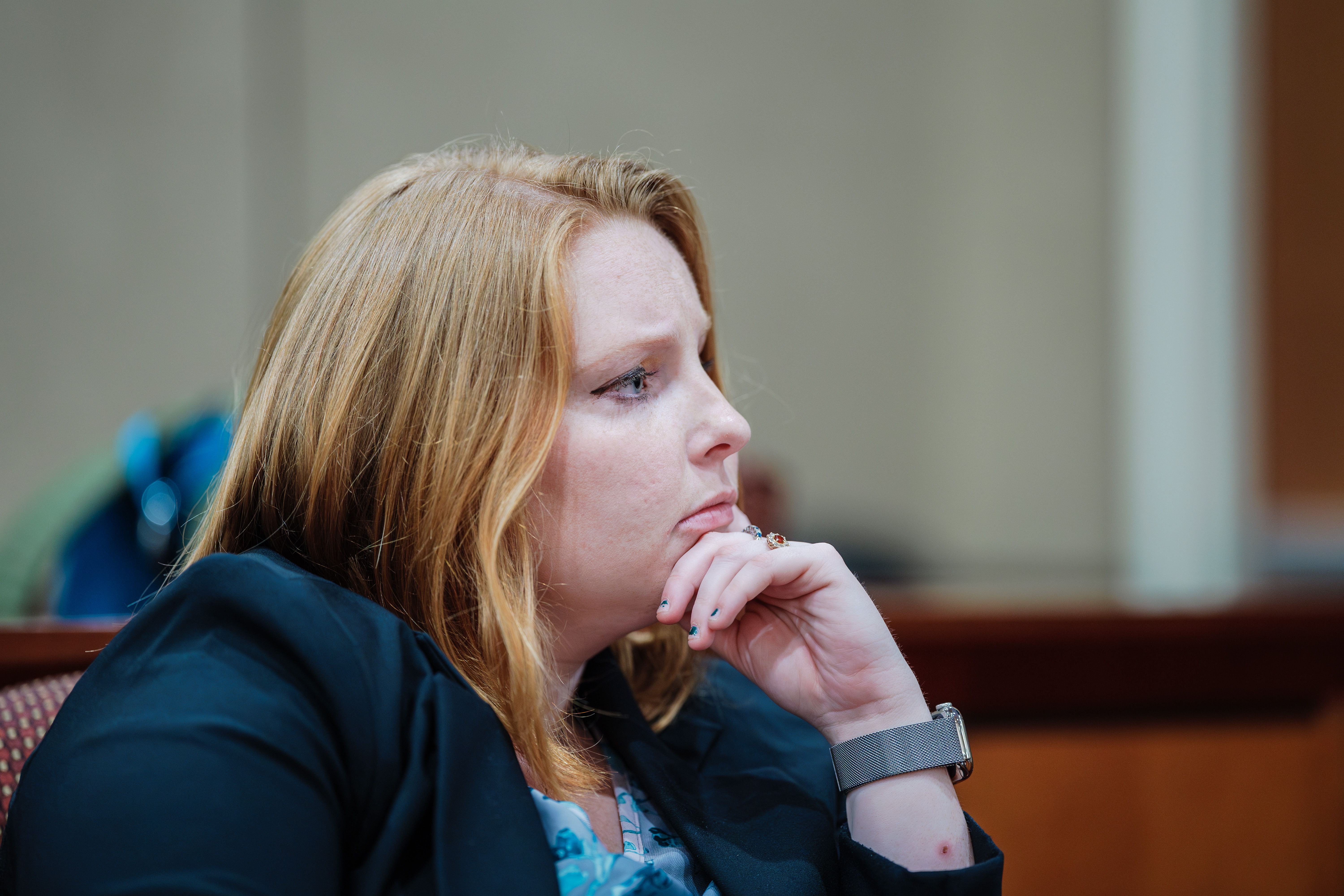 A woman in a courtroom listens intently while holding her chin.
