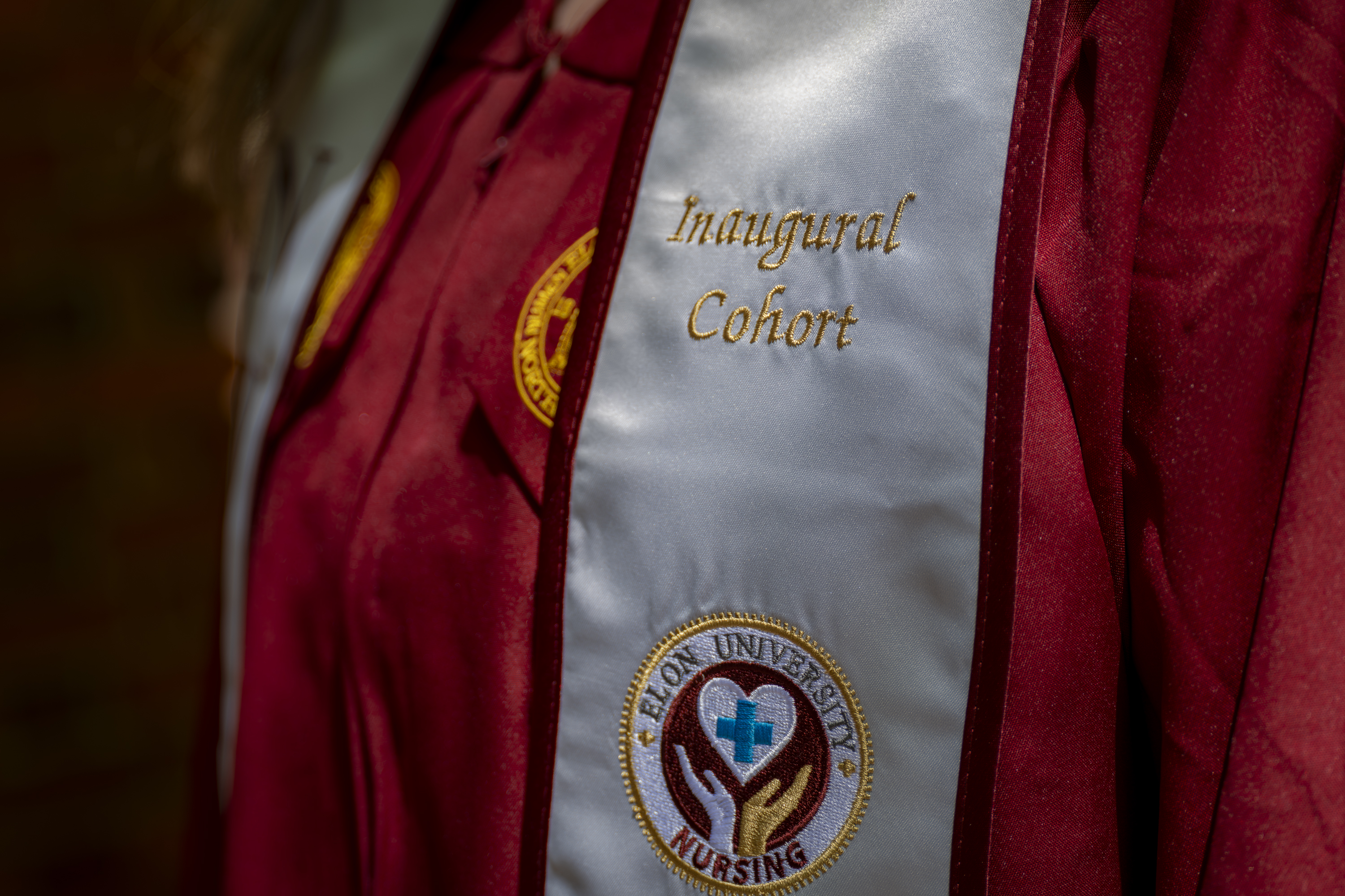 A close-up of a nursing stole embroidered with “Inaugural Cohort” and the Elon University Nursing emblem over a maroon graduation gown.