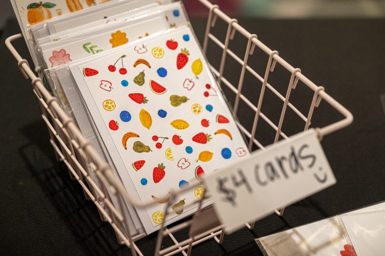 A wire basket holds colorful, fruit-themed greeting cards labeled for sale at $4 each.