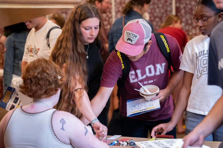 Several students gather around a table, exploring handmade items and activities while chatting with the vendor.