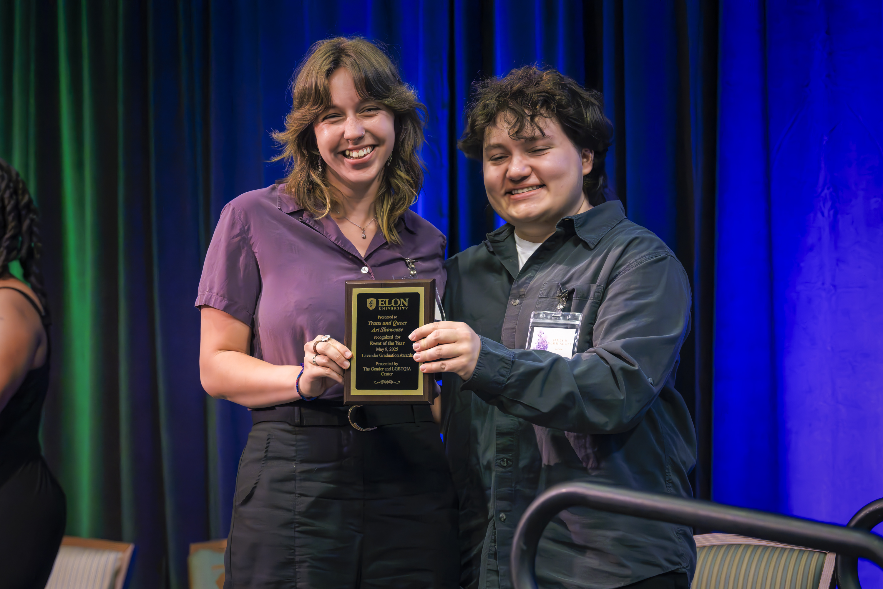 Two students smile and hold up an award plaque together on stage at an Elon University ceremony.