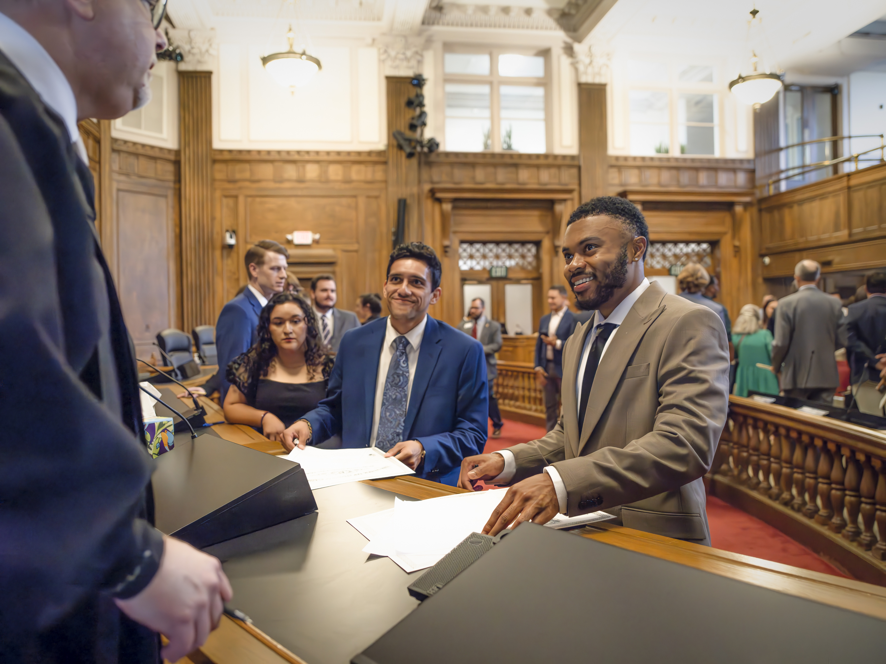 A smiling man in a suit hands a judge documents to be signed.