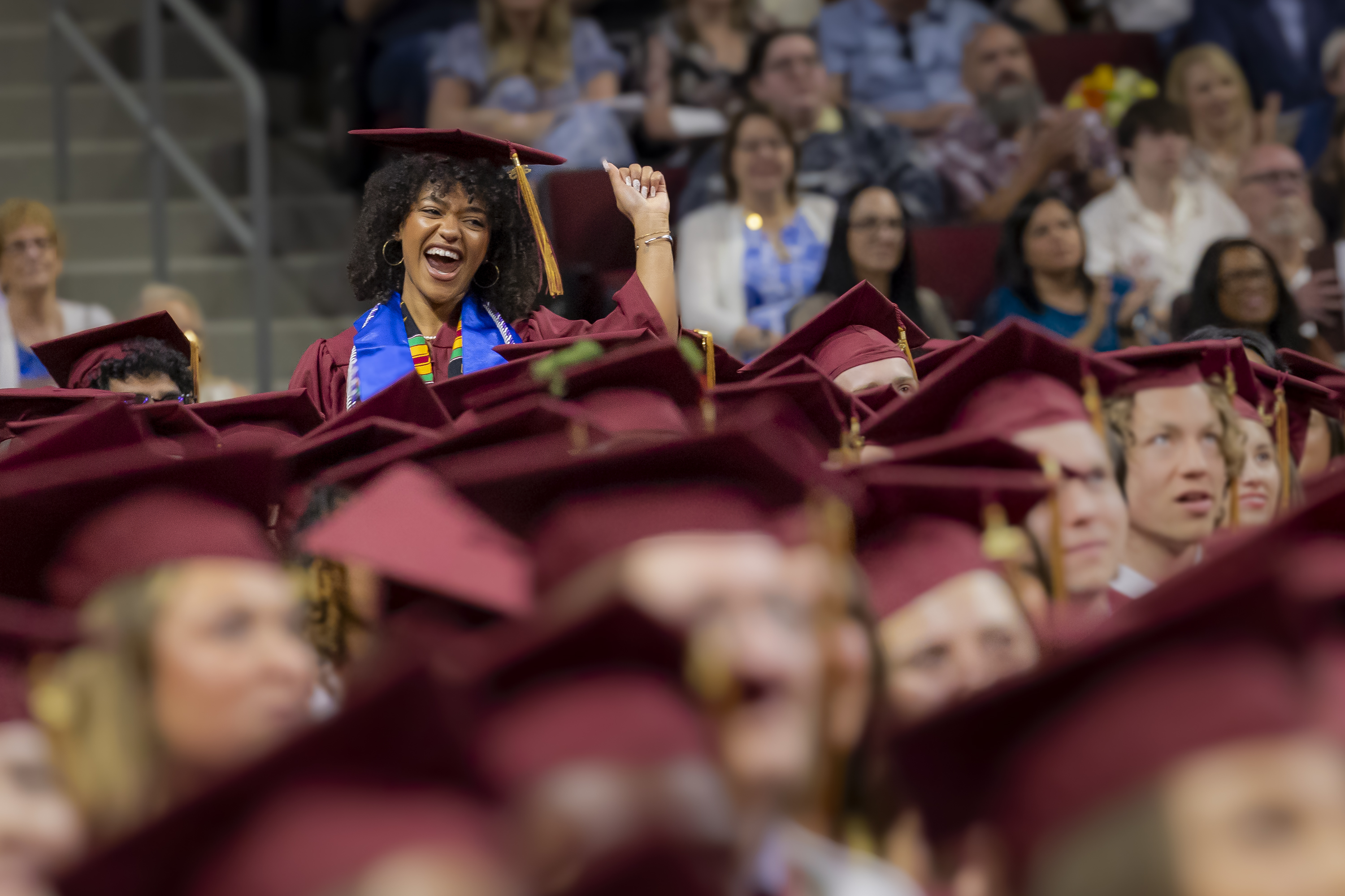 One graduate stands with a fist in the air smiling among a sea of other graduates