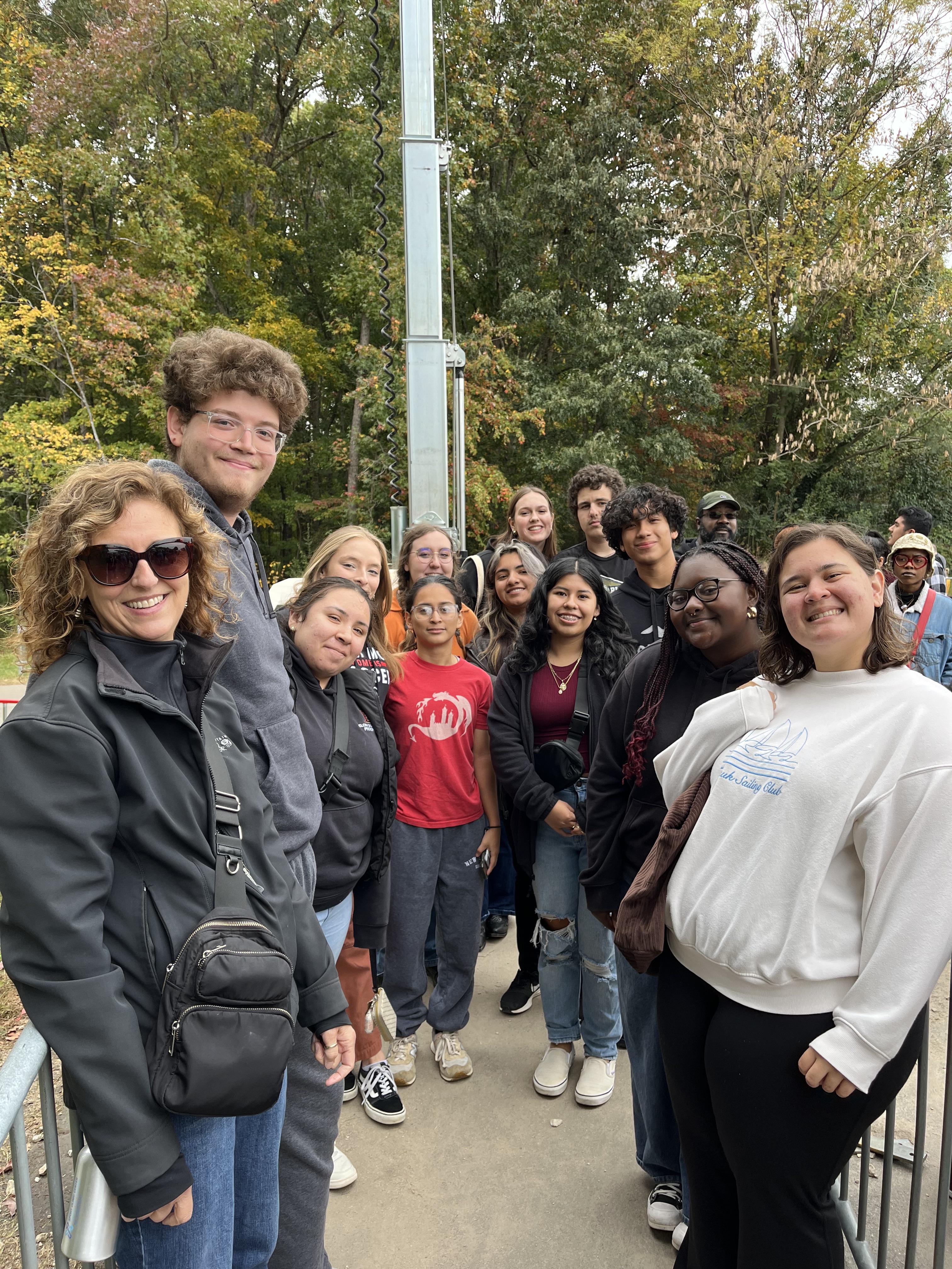 A group of students and a faculty member pose together outside on a tree-lined path, smiling as they prepare for an outing or activity.