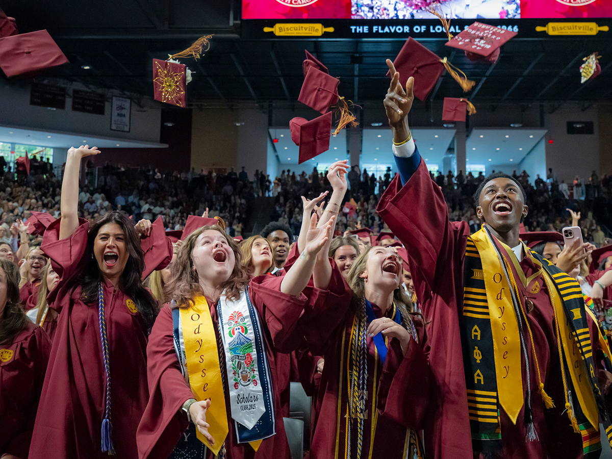 Elon University graduates cheer and toss their caps into the air as Commencement concludes, with excitement filling the arena.
